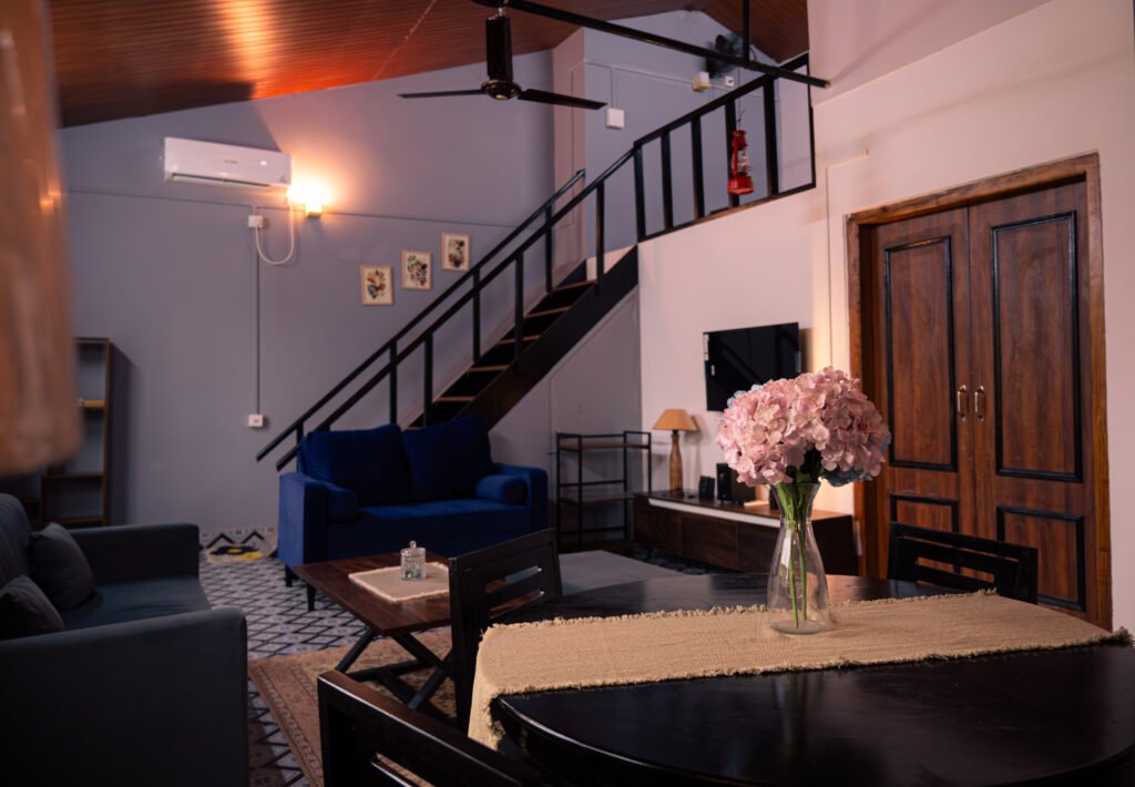 Lounge with stairs, doors, sofa, dining table, vase, AC, and wall shelf.