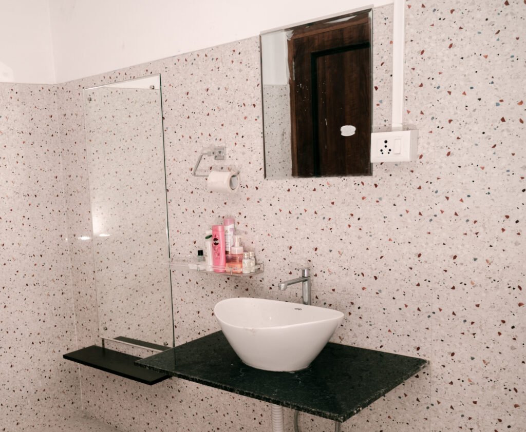 Sink with a shelf holding shampoo and essentials, wall-mounted mirror, tissue paper, and a switchboard