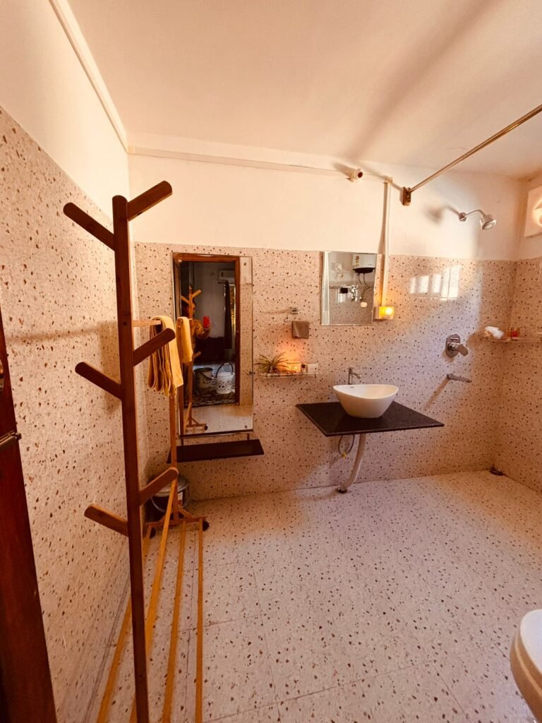 Spacious terrazzo-tiled bathroom with wall-mounted mirror, vessel sink on black countertop, wooden coat rack, and walk-in shower.