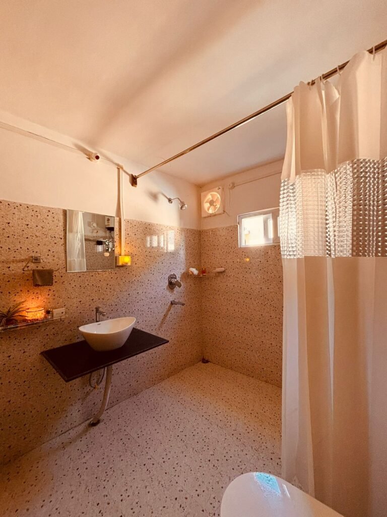 Modern bathroom with terrazzo flooring, wall-mounted black countertop sink, and walk-in shower separated by a white curtain.