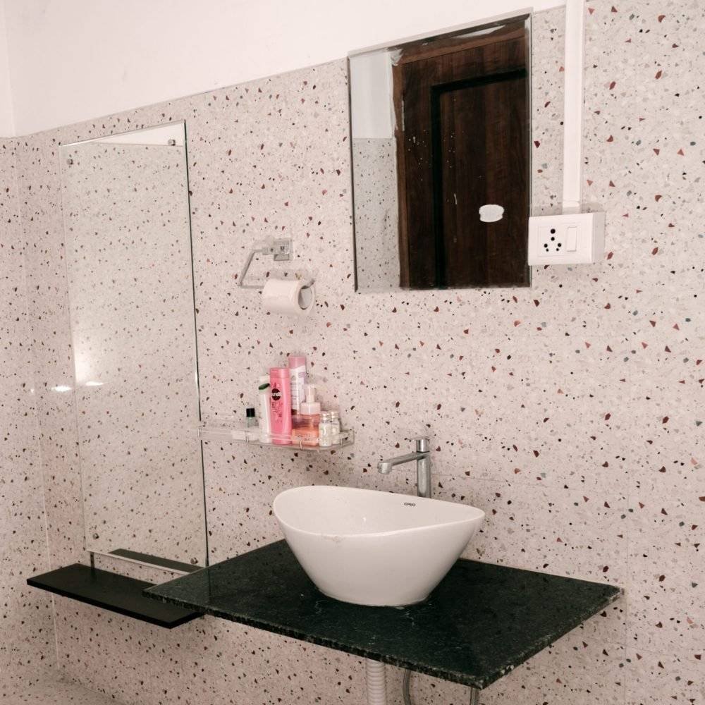 Sink with a shelf holding shampoo and essentials, wall-mounted mirror, tissue paper, and a switchboard